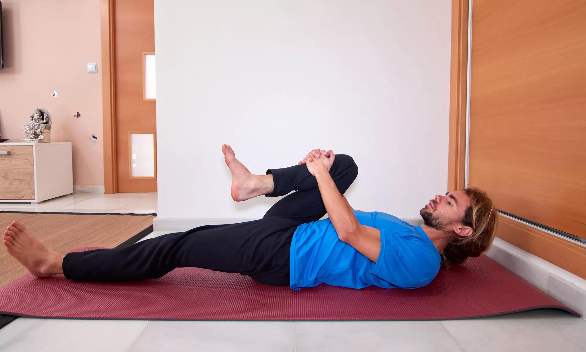 A side view of a Spanish bearded young male in sportswear stretching on the yoga mat at home